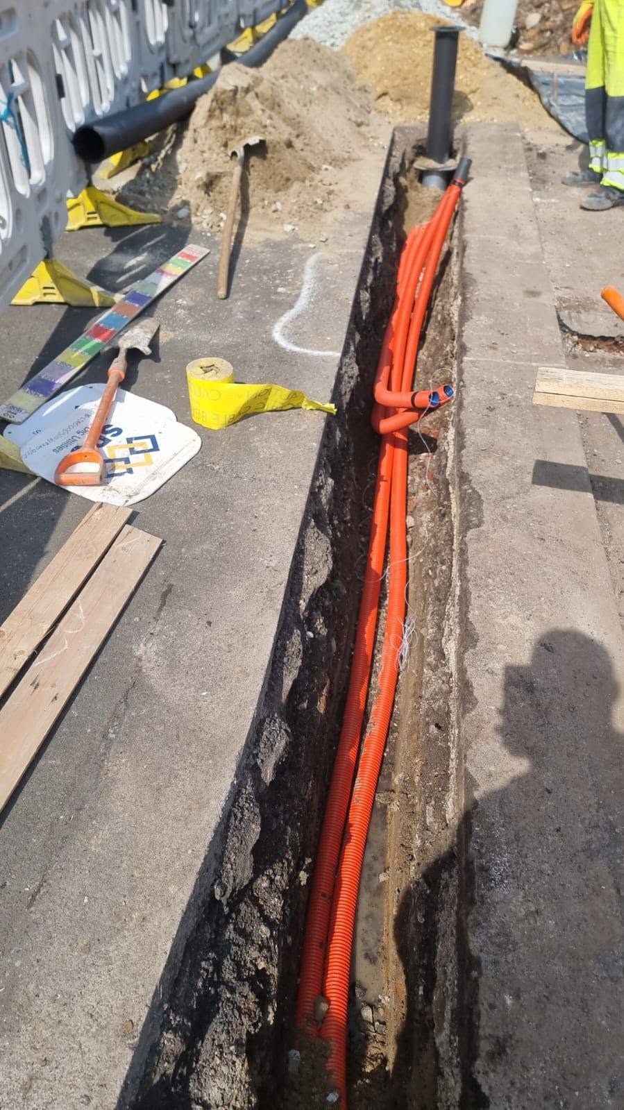 Orange utility ducts laid in a narrow street-side trench
